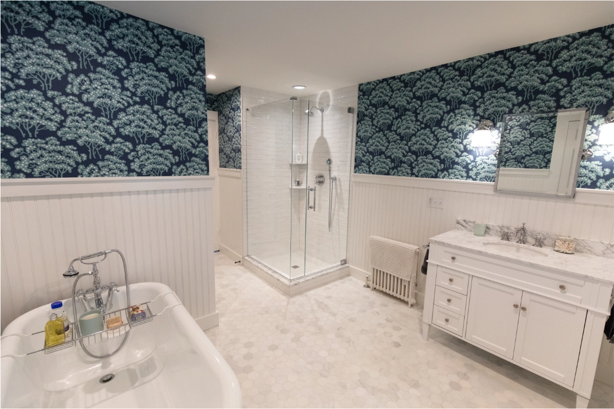 Stylish bathroom with navy floral wallpaper, a glass shower, freestanding tub, and white vanity.
