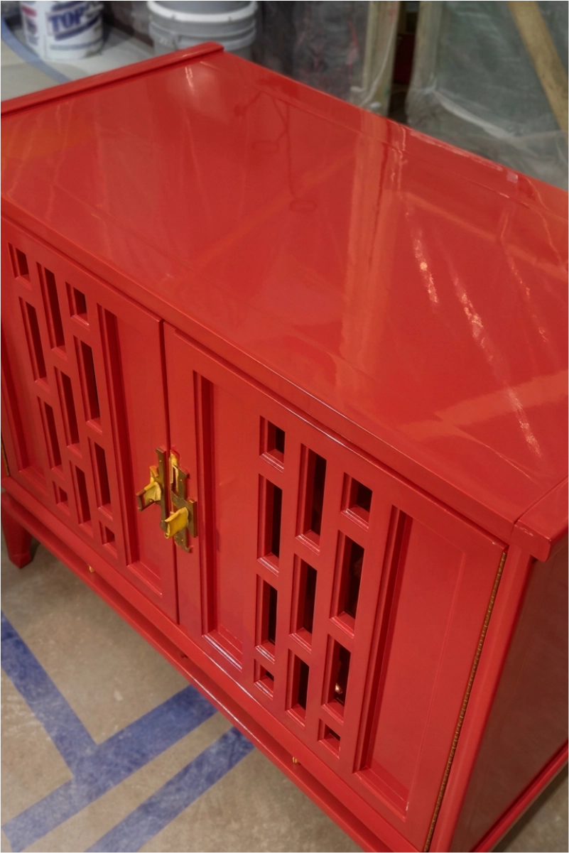 Bright red painted cabinet with geometric cutout doors and gold hardware in a workshop.