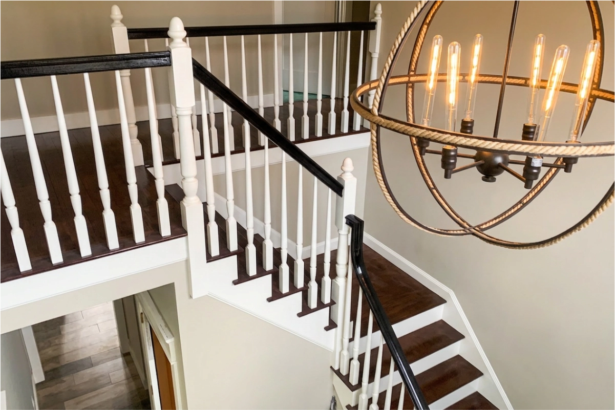 Modern interior staircase with dark wood treads, white balusters, black handrails, and a large circular chandelier